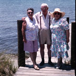 Three elderly people posing together by a waterfront dock.