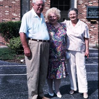 Three elderly individuals posing together outdoors.