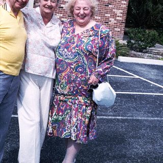 Three elderly people smiling outside brick building.