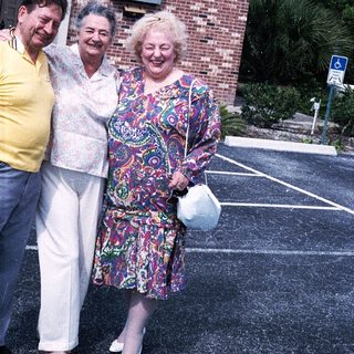 Three elderly people smiling outside brick building.