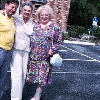Three elderly people smiling outside brick building.