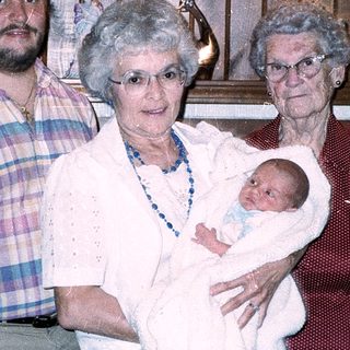 Family portrait with grandparents, adult, and newborn baby.