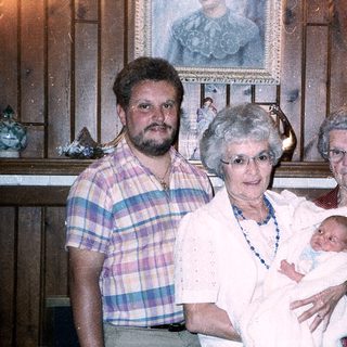 Family portrait with grandparents, adult, and newborn baby.