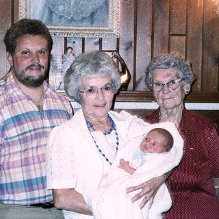 Family portrait with grandparents, adult, and newborn baby.