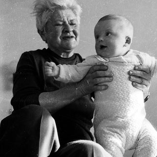 Old woman holding crying baby indoors.