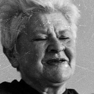 Old woman holding crying baby indoors.