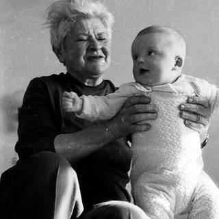 Old woman holding crying baby indoors.