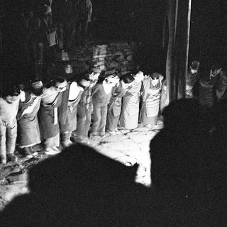 Group of people in traditional attire bowing during nighttime ceremony.