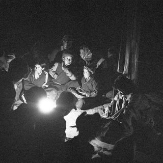 Group gathered indoors by lantern light, appearing to sing or share stories.