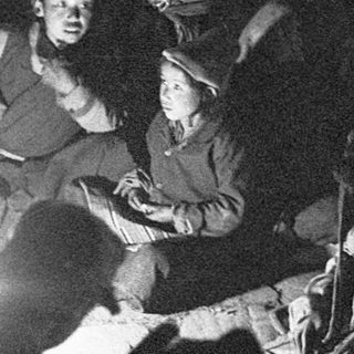 Group gathered indoors by lantern light, appearing to sing or share stories.