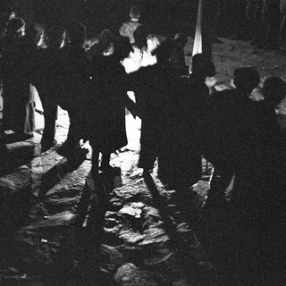 Silhouetted crowd around illuminated bonfire.