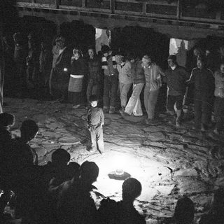 Nighttime gathering around a central figure in a dug pit.