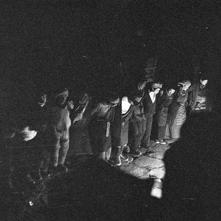 Group of people gathered around candlelight in dark setting.