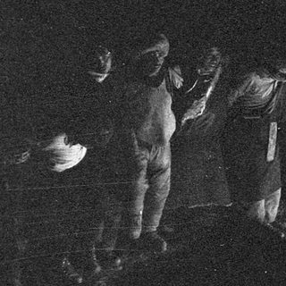 Group of people gathered around candlelight in dark setting.