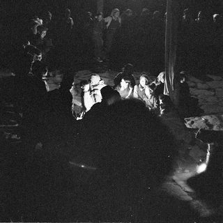 Dark indoor gathering with people watching stage performance.