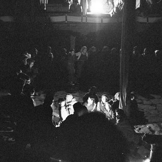 Dark indoor gathering with people watching stage performance.
