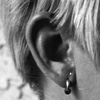 Short-haired person with nose ring and earring.