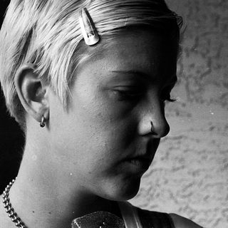 Young person with short hair wearing pearl necklace.