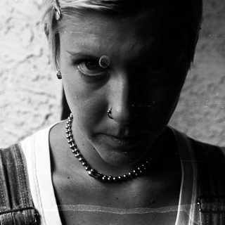 Close-up of person with short hair, piercings, and a beaded necklace.