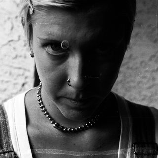 Close-up of person with short hair, piercings, and a beaded necklace.