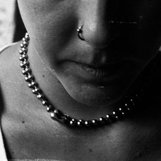 Close-up of person with short hair, piercings, and a beaded necklace.
