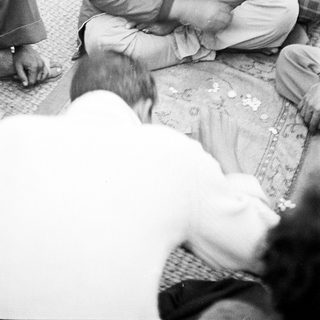 Man shaving another man's beard outdoors.