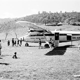 People gather near Royal Nepal Airways seaplane on grass airstrip.