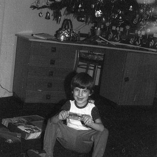 Young boy sitting on floor holding gift box near Christmas tree.