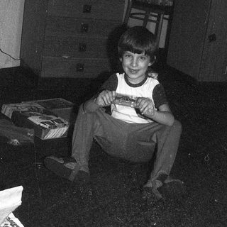 Young boy sitting on floor holding gift box near Christmas tree.
