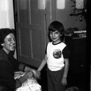 A woman and a young boy shaking hands indoors.