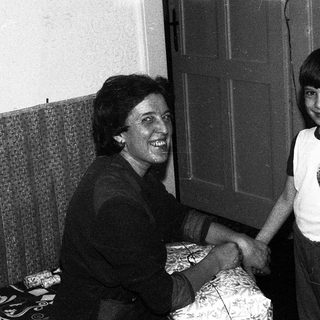 A woman and a young boy shaking hands indoors.
