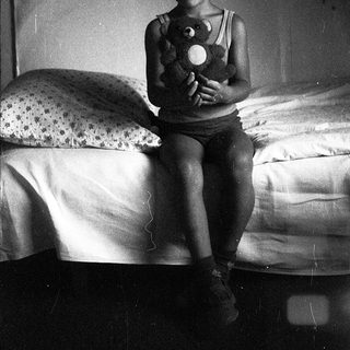 A smiling child holding a stuffed toy on a bed.