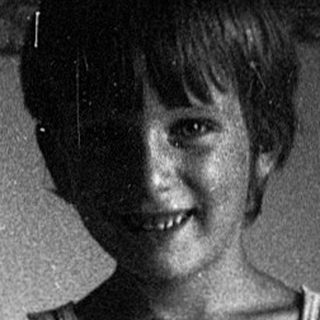 A smiling child holding a stuffed toy on a bed.
