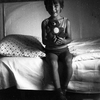 A smiling child holding a stuffed toy on a bed.