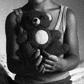 A smiling child holding a stuffed toy on a bed.