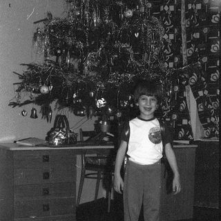 Young boy standing beside decorated Christmas tree.