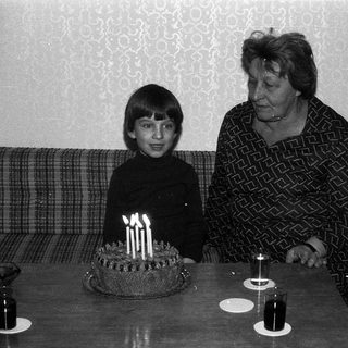 A young boy and elderly woman at a birthday cake with lit candles.