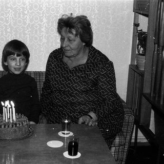A young boy and elderly woman at a birthday cake with lit candles.