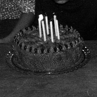 Three children sitting by a birthday cake with lit candles.