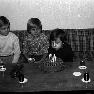 Three children sitting by a birthday cake with lit candles.