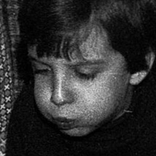 Three children sitting by a birthday cake with lit candles.