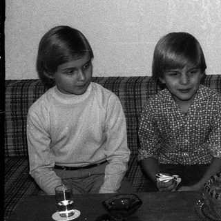 Three children sitting by a birthday cake with lit candles.