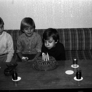 Three children sitting by a birthday cake with lit candles.