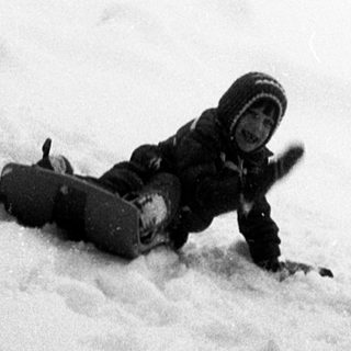 Person snowboarding downhill in snowy forest terrain.