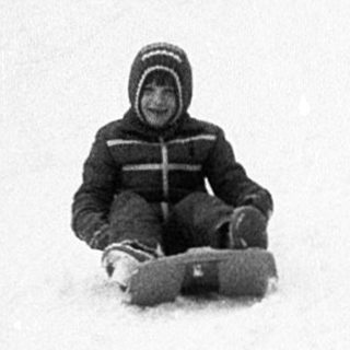 Child sledding down snow-covered hill.
