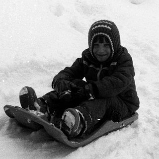Child sledding down snow-covered hill.
