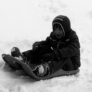 Child sledding down snow-covered slope.