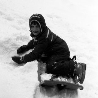 Child joyfully sledding down snow-covered slope.