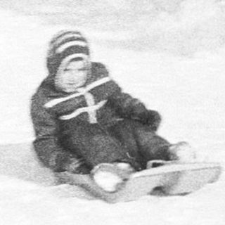 Child sledding down snow-covered slope in park.