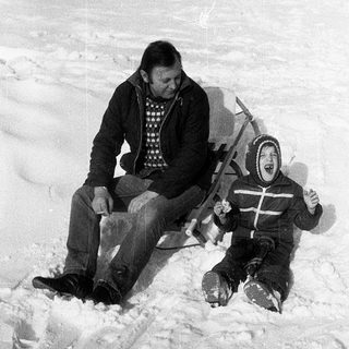 Two people sledding down snow-covered hill.